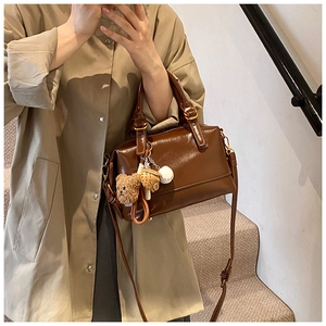 Brown gloss PU leather Boston bag with plush bear charm worn on a shoulder