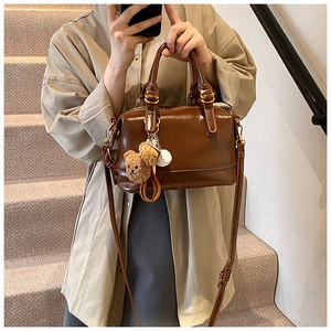 Detail of dark brown glossy Boston bag with gold hardware and cute bear charm pendant