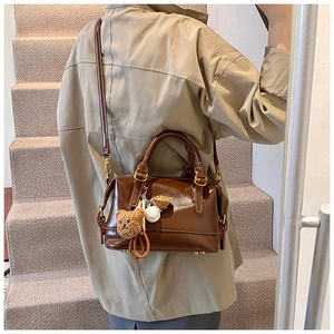 Close-up of brown leather Boston bag with cute plush bear charms and golden hardware