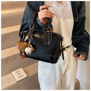Detail of black Boston bag with white contrast stitching and plush bear charm on stairs