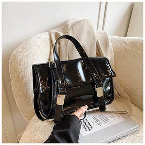 Detail of glossy black messenger bag with silver buckles on a cozy white armchair