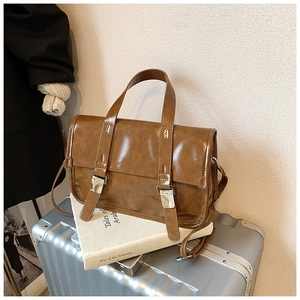 Close-up of retro brown faux leather messenger bag with metal buckles on a silver suitcase