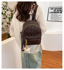 Detail of dark brown embossed backpack with bear pattern and plush monster charm