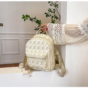Detail of cream mini backpack featuring all-over bear print and fluffy ball keychain