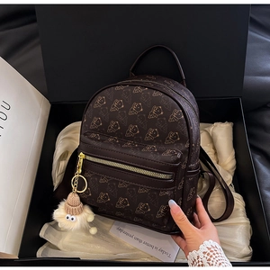 Detail of a brown leather backpack with bear prints and a plush monster charm in a gift box
