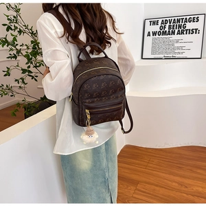 Detail of vintage brown mini backpack with bear pattern and cute monster charm accessory