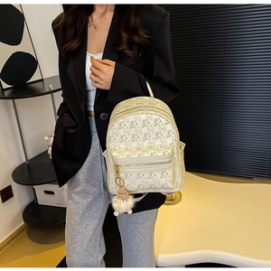 Close-up of off-white backpack featuring embossed bear patterns and a pink pompom charm