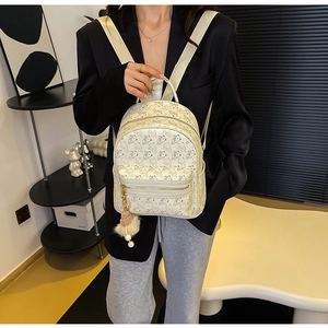 Close-up of mini cream backpack with dark bear prints, gold zipper, and plush ball charm