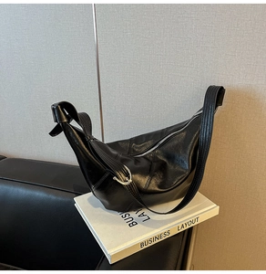 Detail der schwarzen glänzenden Hobo-Tasche mit breitem Schultergurt und Metallring-Dekor