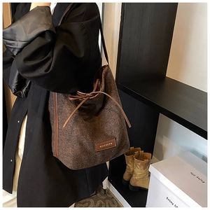 Detail of coffee-colored textured fabric bucket bag with drawstring and leather logo