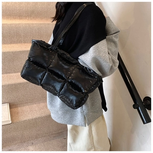 Close-up of a large black quilted tote bag with glossy finish on a shoulder model