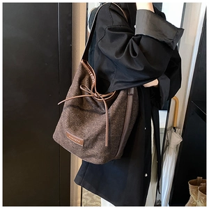Detail of a brown tweed bucket bag with leather trim and drawstring on a black coat