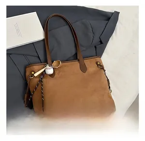 Détail d'un sac cabas en daim marron avec anses en cuir et pendentif de batte de baseball