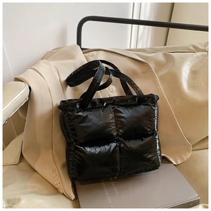 Close-up of black quilted puffer tote bag with glossy finish on stylish beige background