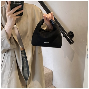Detail der schwarzen Wildlederhandtasche mit silberner Logo-Platte und glattem Ledergriff