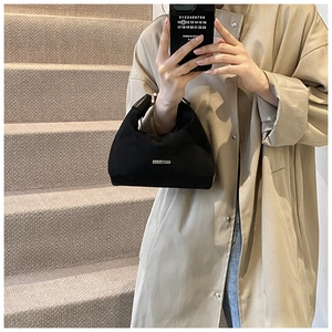 Detail einer schwarzen Halbmond-Handtasche aus Segeltuch mit Logo und beigefarbenem Trenchcoat