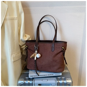 Détail d'un sac cabas en daim marron avec bandoulière en cuir et breloque sur le thème du baseball