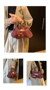 Close-up of burgundy leather Boston bag featuring white contrast stitching and a mini charm