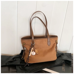 Détail du cabas en daim marron avec anses en cuir et breloque de baseball vintage