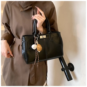 Detail of black leather tote bag with silver twist lock and baseball themed bag charm