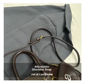 Detail of adjustable leather strap with gold buckle and white embroidery on dark brown bag