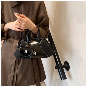 Detail of black bowling bag with white stitching and silver 'a' hardware on a trench coat