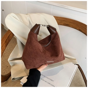 Detaillierte Ansicht der dunkelbraunen Wildlederhandtasche mit silberner Schnalle auf Holzstuhl