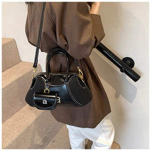 Detail of black glossy shoulder bag featuring white contrast stitching and mini pouch