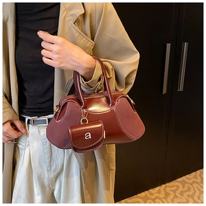 Detail of burgundy leather patchwork bag featuring white contrast stitching and mini charm