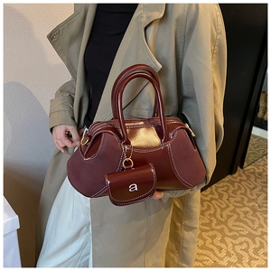Detail of burgundy leather boston bag with white contrast stitching and a letter charm