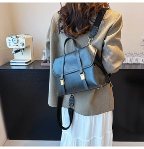Detail view of black matte leather backpack with double strap buckles and woven shoulder strap