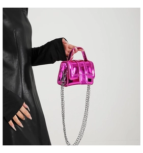 Detail of mini fuchsia metallic handbag with silver chain strap held by model