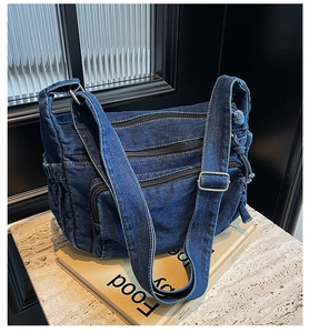Detail of blue denim crossbody bag featuring multiple zipper compartments and fabric texture