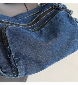 Detail of blue denim shoulder bag showing multiple zipper pockets and white stitching
