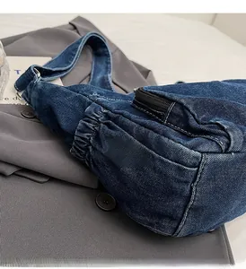 Detail of dark blue denim crossbody bag featuring pleated design and white stitching