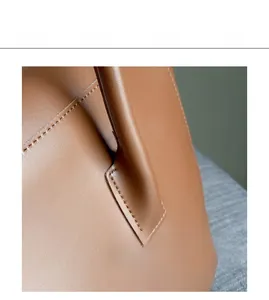 Detail view of smooth brown leather handbag with reinforced stitching and handle attachment
