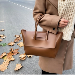 Brown leather tote bag featuring a wide flap and integrated handle in autumn setting