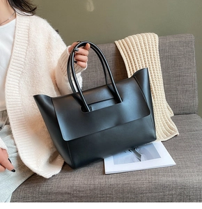 Close-up of a black matte leather tote bag being held by a model in a cozy setting