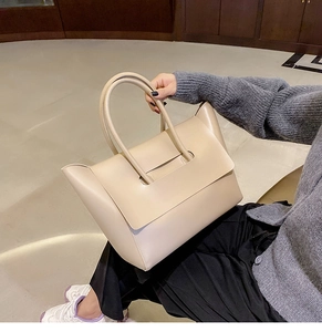 Close-up of a large beige leather tote bag featuring a unique handle through flap design