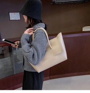 Side view of a large beige leather tote bag worn as a shoulder bag on a female model