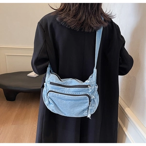 Detailed view of light blue denim crossbody bag with multi-pockets shown on model