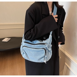 Detail of light blue denim hobo bag with two black zippers and frayed edge accents