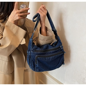Detail of dark blue denim messenger bag showing functional zippers and stitching texture