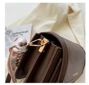 Detailansicht der braunen Ledertasche mit goldener Hardware und gepunktetem Seidentuch