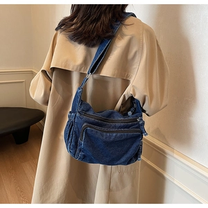 Detailed view of dark blue denim messenger bag with multiple functional zippers on back