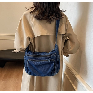 Detail view of retro denim messenger bag showing layered zippers and wide shoulder strap