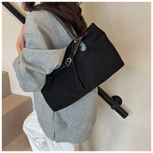 Detailed view of spacious black tote bag featuring leather straps and side pendant