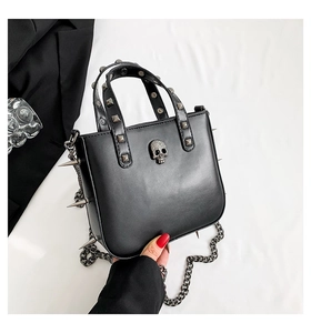 Close-up of gothic punk handbag featuring metal skull and rivets on black leather surface