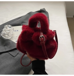 Détail du sac seau en peluche rouge avec poignée en cuir sur une veste de costume grise