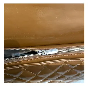 Detail of silver metal zipper on brown quilted leather bag with diamond stitching texture